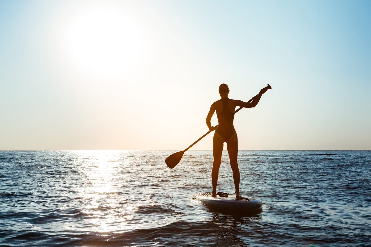 Silhouette of young beautiful girl surfing in sea at sunrise. Outdoors.
